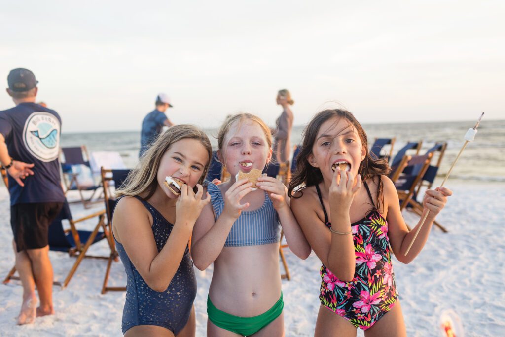 Three girls eating s'mores on sandy beach