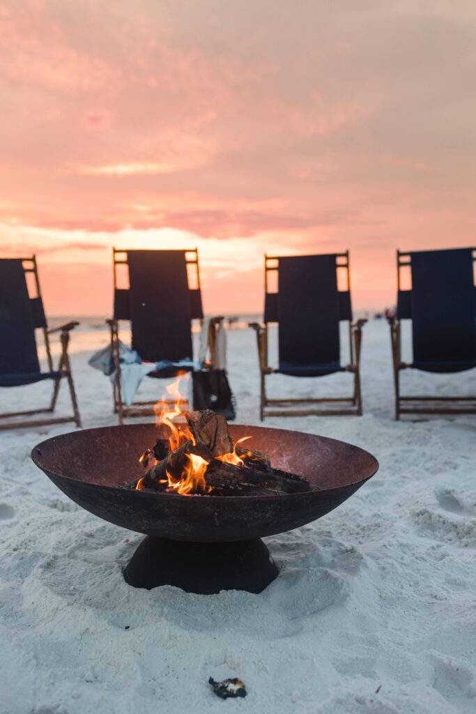 A fire pit on the beach with chairs in front of it.