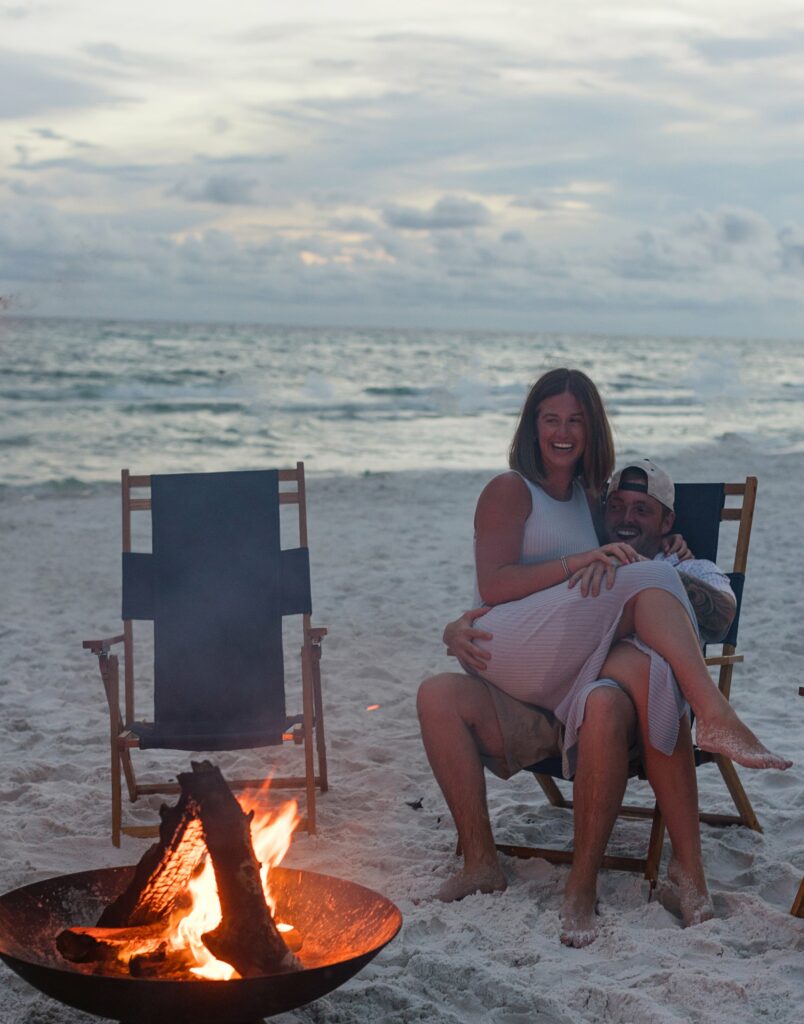 A man and woman sitting on lawn chairs next to fire.