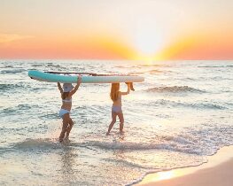 Two people carrying surfboard on beach at sunset